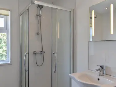 a white bathroom with a shower and a sink at 1 Merope in Padstow