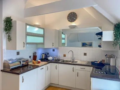 a kitchen with white cabinets and a clock on the wall at The Watch House in Saint Mawes