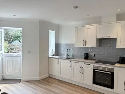 a white kitchen with white cabinets and a window at La Mouette in Mevagissey