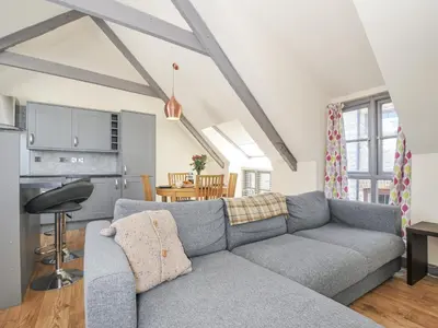 a living room with a gray couch and a kitchen at Beach Retreat in Looe