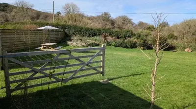 a fence in a yard with a table and an umbrella at St Ives Countryside Home with Pool Table & Parking in Towednack