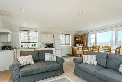 a living room with two couches and a kitchen at Arnold Cottage in St Merryn