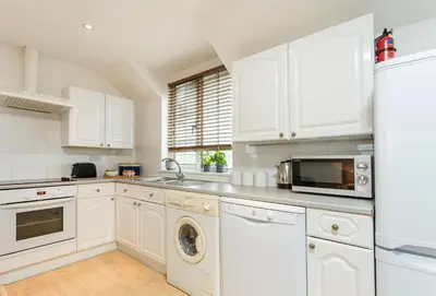 a kitchen with white cabinets and a washer and dryer at Arnold Cottage in St Merryn
