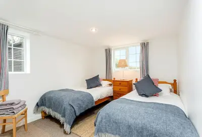 two beds in a room with white walls and windows at Arnold Cottage in St Merryn