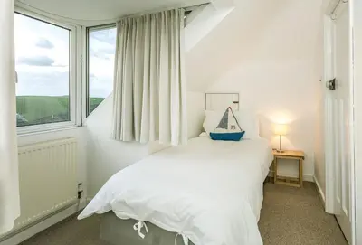 a white bedroom with a bed and a window at Bay View in Port Isaac