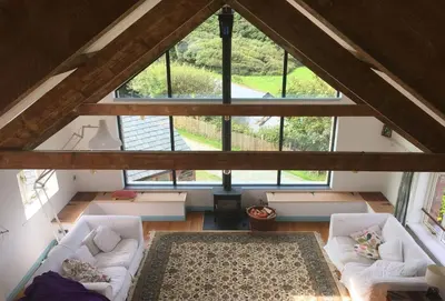 an attic room with white couches and a large window at Lower Hillcott in Bude
