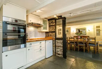 a kitchen with white cabinets and a dining room at Primrose Cottage in St Merryn