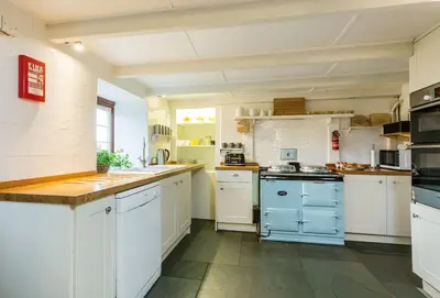 a large kitchen with white cabinets and blue appliances at Primrose Cottage in St Merryn