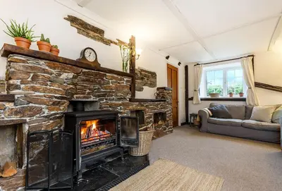 a living room with a stone fireplace and a couch at Primrose Cottage in St Merryn