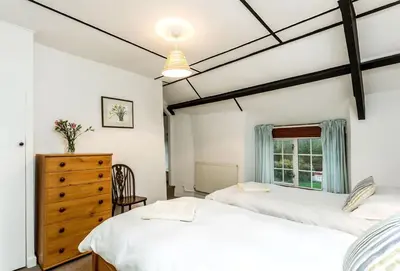 two beds in a bedroom with a dresser and a window at Primrose Cottage in St Merryn