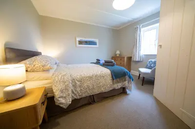 a bedroom with a bed and a chair at Penrose Cottage in Bude