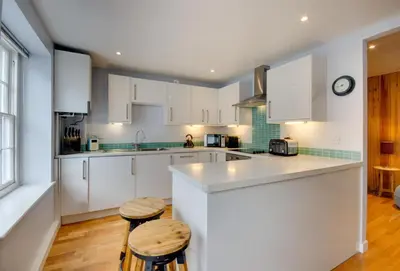 a kitchen with white cabinets and two stools at Quayside in Fowey