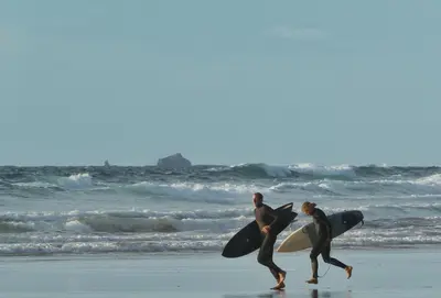 two men walking on the beach with their surfboards at The Treyarnon Suite in St Merryn