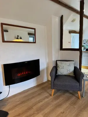 a living room with a fireplace and a chair at Titmouse at Trenale Court Cottages in Tintagel