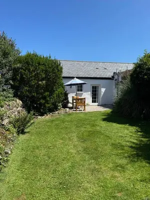 a white house with an umbrella in the yard at Titmouse at Trenale Court Cottages in Tintagel