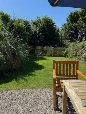 a wooden bench sitting next to a yard with a fence at Titmouse at Trenale Court Cottages in Tintagel