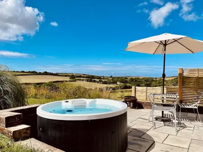 a hot tub and an umbrella on a patio at The Dairy - Luxurious Hideaway on The Lizard in Cury