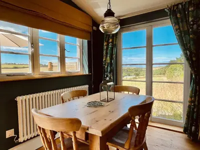 a dining room with a wooden table and chairs and windows at The Dairy - Luxurious Hideaway on The Lizard in Cury