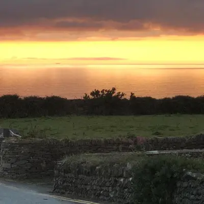 a sunset over the ocean with a stone wall at Pendrin Guest House in Tintagel