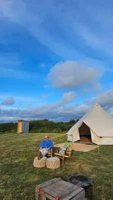 a man sitting on a log in front of a tent at Tiny Treamble in Cubert
