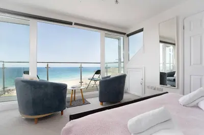 a bedroom with a bed and two chairs and the ocean at Trewirgie in St Ives