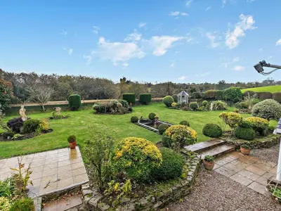 a garden with a large lawn with bushes and trees at Rose Cottage in Saint Hilary