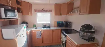 a kitchen with wooden cabinets and a white refrigerator at 5Berth -Family Friendly -ParkingSpot -Heated Pool in St Austell