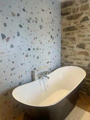 a bath tub in a bathroom with a stone wall at Honeysuckle Cottage in St. Agnes