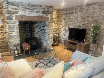 a living room with a stone fireplace and a tv at Honeysuckle Cottage in St. Agnes