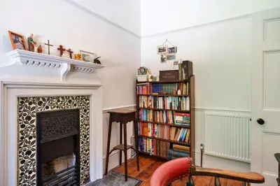 a living room with a fireplace and a book shelf filled with books at Finest Retreats - The Old Vicarage in Talland