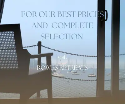 a chair in front of a window with a view of a beach at Merchants House in Penryn