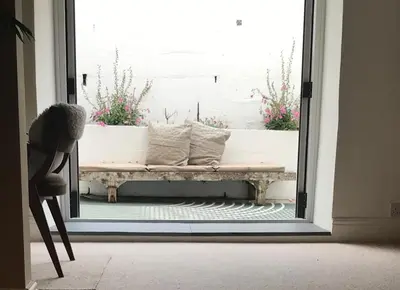 a bench sitting outside a door with flowers in a window at April Cottage in Saint Erth
