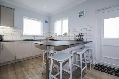 a kitchen with white cabinets and a island with stools at Pipers in Newquay