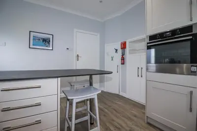 a kitchen with white cabinets and a counter with a stool at Pipers in Newquay