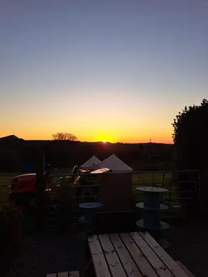 a sunset with a table and tents in a field at Bell Tent 2 in St Austell