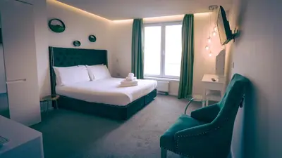 a bedroom with a bed and a chair and a window at The Feather's Hotel Newquay in Newquay