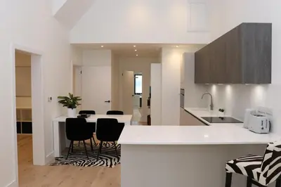 a white kitchen with black chairs and a counter at The Hidden Sanctuary in Stithians