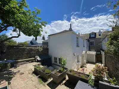 a white house with potted plants in a yard at Central, 10min walk to beach with off-road parking in Falmouth