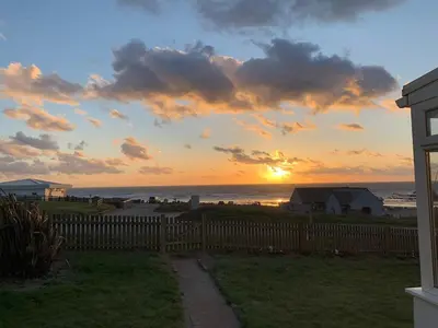 a sunset over the ocean with a wooden fence at Bungalow with stunning views over Widemouth Bay in Widemouth Bay