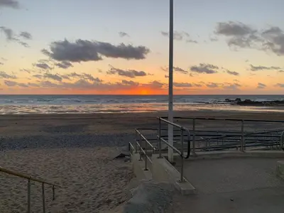 a sunset at the beach with a bench and the ocean at Bungalow with stunning views over Widemouth Bay in Widemouth Bay