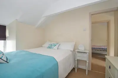 a white bedroom with a bed and a mirror at 2 Porthilly Cottages in Wadebridge