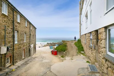 a man walking down a dirt road near the ocean at White Mist Cottage in St Ives
