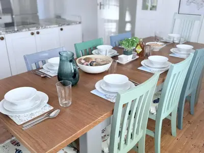 a wooden table with plates and bowls and chairs at Meadow View - Widemouth Bay Cornwall in Widemouth Bay