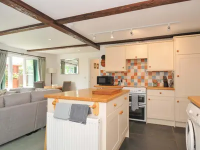 a kitchen and living room with white cabinets and a couch at Upper Court Cottage in Bude