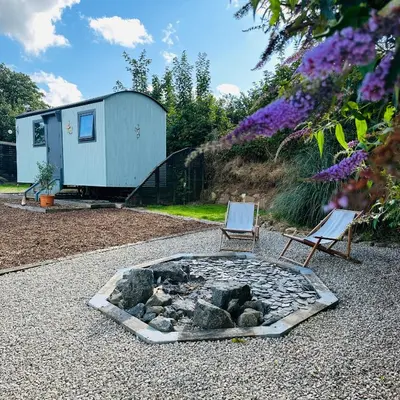a fire pit in a gravel yard with two chairs at Harpers Huts in Lanivet