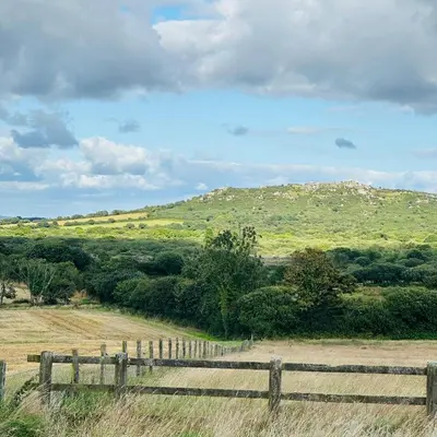 a fence in a field with a hill in the background at Harpers Huts in Lanivet