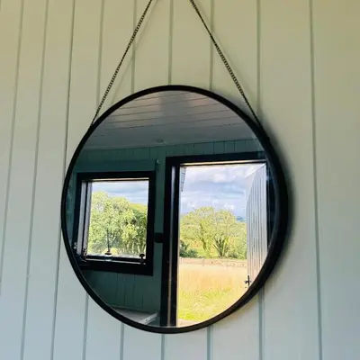a mirror hanging on a wall with a window at Harpers Huts in Lanivet