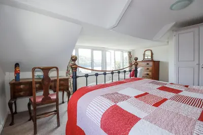 a bedroom with a bed and a chair and a window at Kiln Cottage in Fowey