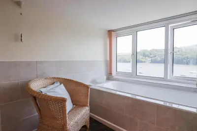 a bathroom with a tub and a chair and a window at Kiln Cottage in Fowey