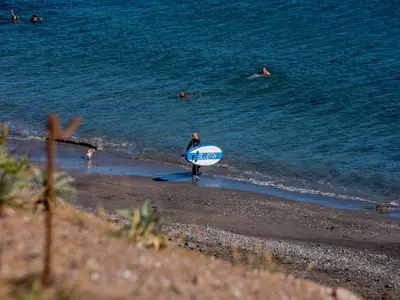a man walking on the beach with a surfboard at On The Beach in Downderry